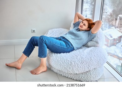 New dwelling for shoeless woman who lies on bean bag chair near floor to ceiling window. - Shutterstock ID 2138751669