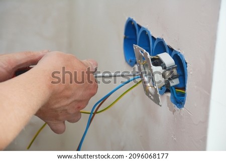 New electrical socket installation. An electrician is attaching a new power outlet with power wires to the electrical box, screwing the outlet receptacle, power socket in place.