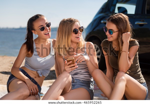New emotions.\
Cheerful delighted smiling friends sitting on the sand and using\
laptop while resting\
together