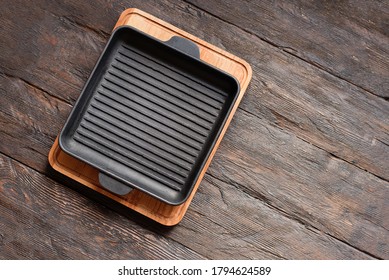 New Empty Cast-iron Grill Pan With Two Handles On Wooden Background. Place For Text. Flat Lay Top View Black Cast Iron Skillet For Barbecue. Food Mockup