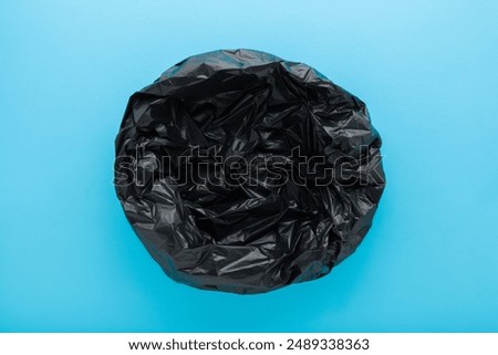 New empty dark black opened plastic garbage bag on light blue table background. Pastel color. Closeup. Top view.