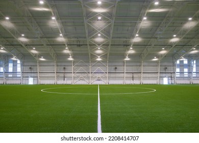 A new empty European sports hall for playing football at any time of the year. The football field is covered with artificial grass, lighting spotlights are installed on the walls and ceiling. - Powered by Shutterstock