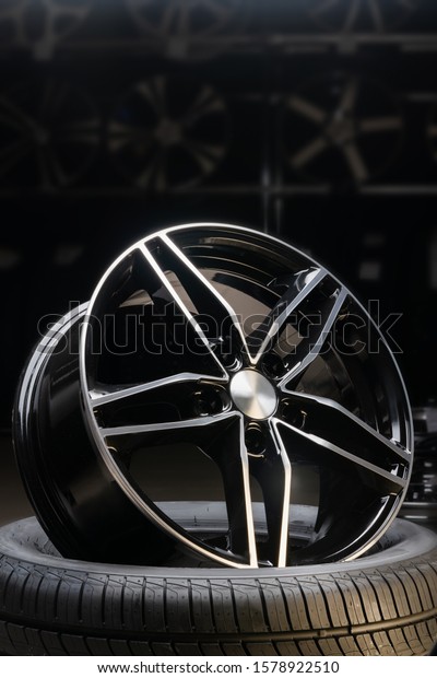 new expensive cast aluminum disc wheel black color,\
photographed on the tire. dark background, close-up. vertical\
layout, glare from above
