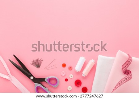New fabric, thread spools, zipper, needles, buttons and dressmaker scissors. Kit for female clothes sewing on light pink table background. Pastel color. Closeup. Empty place for text. Top view.
