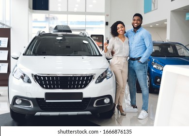 New Family Car. Cheerful Husband And Wife Holding New Automobile Key Smiling To Camera Standing Near Auto In Dealership Shop.