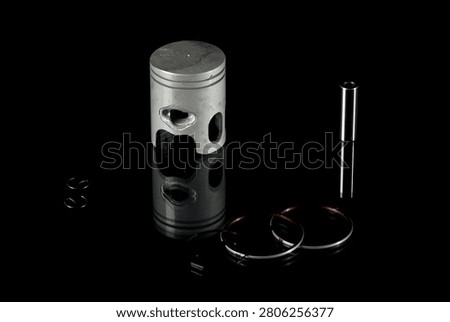 New four-stroke engine piston assembly kit isolated on black background. Motorcycle, scooter or ATV powertrain repair parts set including aluminum piston, wrist pin, compression rings, oil scraper ring components and circlips. Studio low-key macro shot.