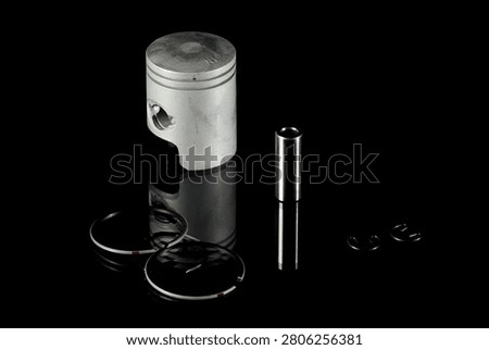 New four-stroke engine piston assembly kit isolated on black background. Motorcycle, scooter or ATV powertrain repair parts set including aluminum piston, wrist pin, compression rings, oil scraper ring components and circlips. Studio low-key macro shot.