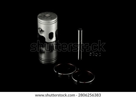 New four-stroke engine piston assembly kit isolated on black background. Motorcycle, scooter or ATV powertrain repair parts set including aluminum piston, wrist pin, compression rings, oil scraper ring components and circlips. Studio low-key macro shot.