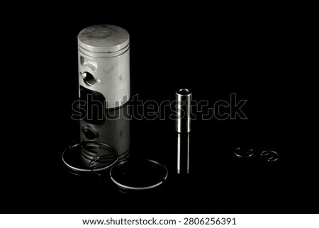 New four-stroke engine piston assembly kit isolated on black background. Motorcycle, scooter or ATV powertrain repair parts set including aluminum piston, wrist pin, compression rings, oil scraper ring components and circlips. Studio low-key macro shot.
