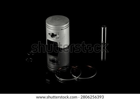 New four-stroke engine piston assembly kit isolated on black background. Motorcycle, scooter or ATV powertrain repair parts set including aluminum piston, wrist pin, compression rings, oil scraper ring components and circlips. Studio low-key macro shot.