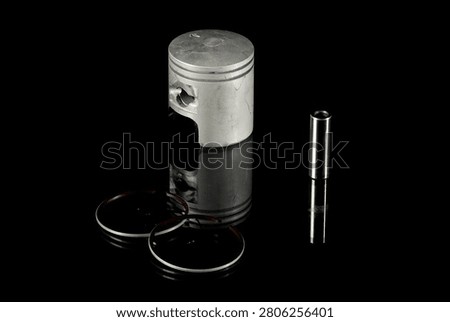 New four-stroke engine piston assembly kit isolated on black background. Motorcycle, scooter or ATV powertrain repair parts set including aluminum piston, wrist pin, compression rings, oil scraper ring components and circlips. Studio low-key macro shot.
