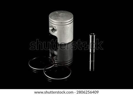 New four-stroke engine piston assembly kit isolated on black background. Motorcycle, scooter or ATV powertrain repair parts set including aluminum piston, wrist pin, compression rings, oil scraper ring components and circlips. Studio low-key macro shot.
