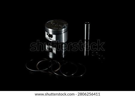 New four-stroke engine piston assembly kit isolated on black background. Motorcycle, scooter or ATV powertrain repair parts set including aluminum piston, wrist pin, compression rings, oil scraper ring components and circlips. Studio low-key macro shot.