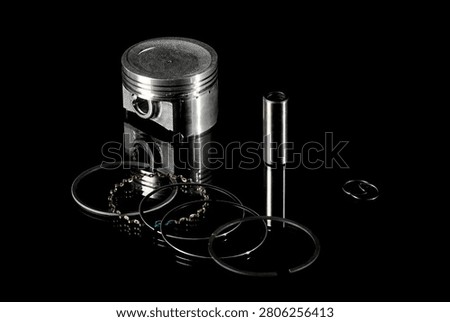 New four-stroke engine piston assembly kit isolated on black background. Motorcycle, scooter or ATV powertrain repair parts set including aluminum piston, wrist pin, compression rings, oil scraper ring components and circlips. Studio low-key macro shot.