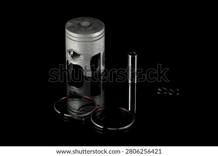 New four-stroke engine piston assembly kit isolated on black background. Motorcycle, scooter or ATV powertrain repair parts set including aluminum piston, wrist pin, compression rings, oil scraper ring components and circlips. Studio low-key macro shot.