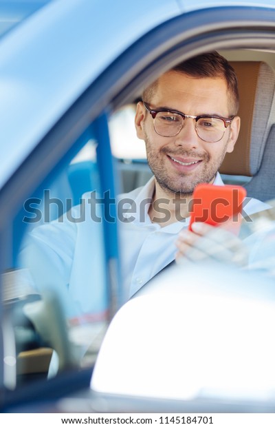 New generation. Delighted handsome man\
using his mobile device while driving in the\
car