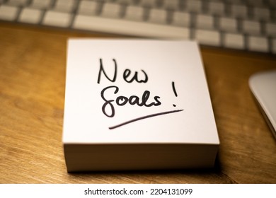 New Goals, Text Note. Office Desk With Notepad And Keyboard In The Background. In Black The Handwritten Text, New Goals. Motivation, Inspiration And Encouragement.