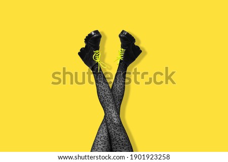 New gray female boots with bright yellow laces on long slender crossed woman legs in gray tights isolated on yellow background. Pop art concept with Heavy Duty Boots. Banner with copy space.