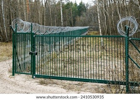 A new green metal mesh fence with coiled barbed wire and gate around the restricted area of a military facility, coiled barbed wire fencing