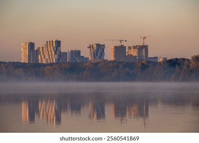 New high-rise buildings with cranes on the shore of a foggy lake. - Powered by Shutterstock