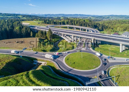 New highway in Poland on national road no 7, E77, called Zakopianka.  Overpass junction with a traffic circle, viaducts, slip roads, cars near Skomielna Biala. Aerial view. Far view of Tatra Mountains
