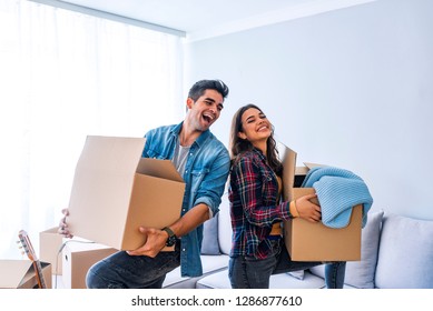 New Home. Funny Young Couple Enjoy And Celebrating Moving To New Home. Happy Couple At Empty Room Of New Home. Happy Couple Is Having Fun With Cardboard Boxes In New House At Moving Day. 