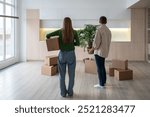 New home owners with boxes and houseplant in hands, rear view. Family couple taking things to another rented light apartment. Housewarming in mortgage apartment. Beginning of happy married life.