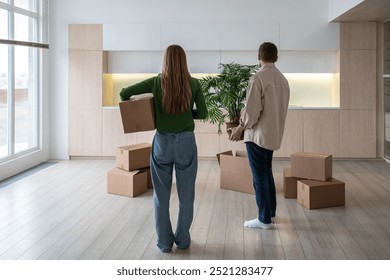 New home owners with boxes and houseplant in hands, rear view. Family couple taking things to another rented light apartment. Housewarming in mortgage apartment. Beginning of happy married life. - Powered by Shutterstock