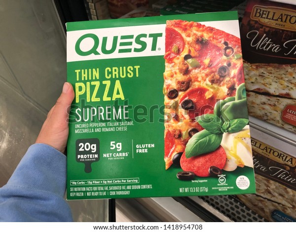 New Hope, Minnesota - May 30,\
2019: Hand holds up a Quest thin crust supreme frozen pizza while\
shopping at a grocery store. This is a low-carb healthy\
pizza