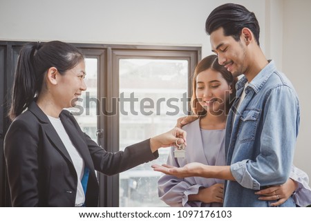 new house / home moving and relocation concept. Happy asian couple receiving apartment key from real estate agent / realtor.