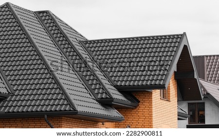 A new house made of yellow bricks and a beautiful black roof. Black corrugated metal profile roof installed on a modern house.