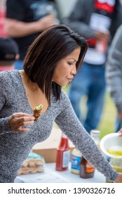 NEW IBERIA, L.A. / USA - FEBRUARY 28, 2015: A Middle-aged Cambodian Female Holding A Jalapeño Popper At A Food Table Placed Outdoors For A Birthday Party In South Louisiana.