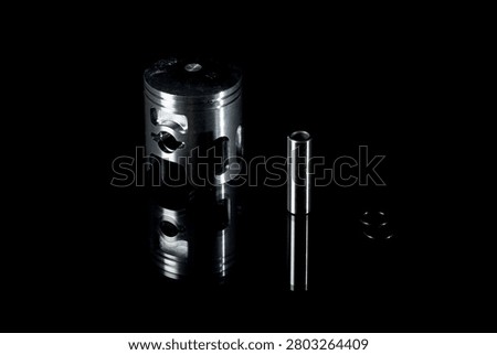 New internal combustion engine piston kit isolated on black background. Motorcycle or scooter two-stroke motor piston assembly with wrist pin, piston rings and circlips. Low-key studio shot of motorbike engine cylinder powertrain replacement parts.