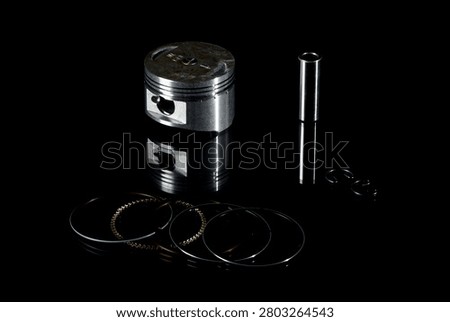 New internal combustion engine piston kit isolated on black background. Motorcycle or scooter two-stroke motor piston assembly with wrist pin, piston rings and circlips. Low-key studio shot of motorbike engine cylinder powertrain replacement parts.