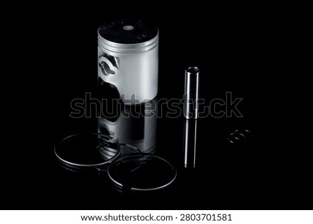 New internal combustion engine piston kit isolated on black background. Motorcycle or scooter two-stroke motor piston assembly with wrist pin, piston rings and circlips. Low-key studio shot of motorbike engine cylinder powertrain replacement parts.