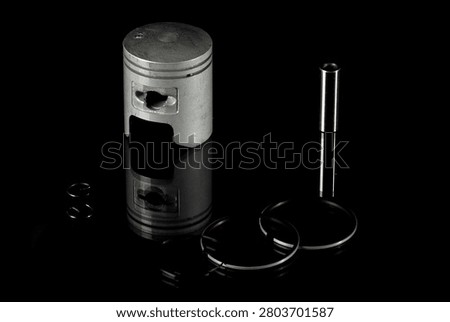 New internal combustion engine piston kit isolated on black background. Motorcycle or scooter two-stroke motor piston assembly with wrist pin, piston rings and circlips. Low-key studio shot of motorbike engine cylinder powertrain replacement parts.