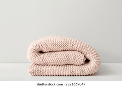 New knitted folded blanket on table near light wall - Powered by Shutterstock - Get 15% off with code: PIKWIZARD15