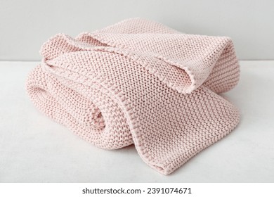 New knitted folded blanket on table near light wall