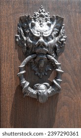 New knocker in the shape of devil's head on wooden door close up