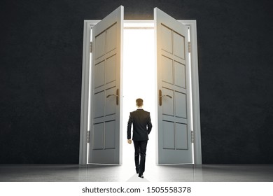 New Life Beginning Concept With Businessman Entering Open White Doors In Abstract Bright Space.