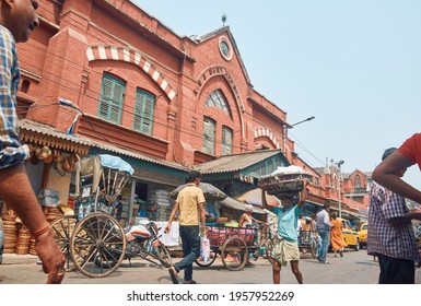 New Market, Kolkata, 03-27-2021: Low Angle View Of A Middle Aged Manual Labour Carrying Basket Filled Goods On His Head, Walking Though Congested Street Near The Iconic Hog Market, A Heritage Building