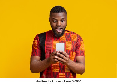 New mobile app. Amazed black guy in authentic t-shirt looking at smartphone screen over yellow background