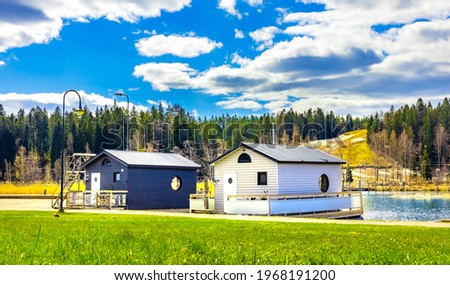 New modern cottages on water in Porvoo, Finland. Two small wooden houses under blue sky with white clouds at sunny day. Bright green lawn in front, pine trees forest behind. Cabin to relax in nature.