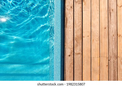 New modern fiberglass plastic swimming pool entrance step with clean fresh refreshing blue water on bright hot summer day at yard or resort hotel spa area. Wooden flooring deck of teak or larch board