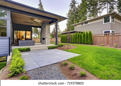 New modern home features a backyard with covered patio accented with stone fireplace, vaulted ceiling with skylights and furnished with gray wicker sofa placed on concrete floor. Northwest, USA 