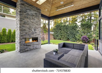 New modern home features a backyard with covered patio accented with stone fireplace, vaulted ceiling with skylights and furnished with gray wicker sofa placed on concrete floor. Northwest, USA  - Shutterstock ID 719378830
