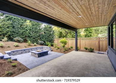 New modern home features a backyard with covered patio accented with a wood plank ceiling and a rectangular fire pit, made of concrete and slate tiles. Northwest, USA