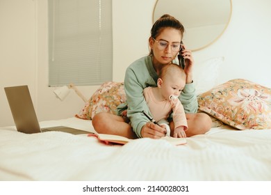 New Mom Taking A Phone Call While Working From Home. Working Mom Making Plans With Her Clients While Sitting On A Bed With Her Baby. Single Mother Balancing Work And Motherhood.