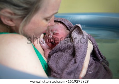 A new mother embracing her newborn baby after a natural pool home birth