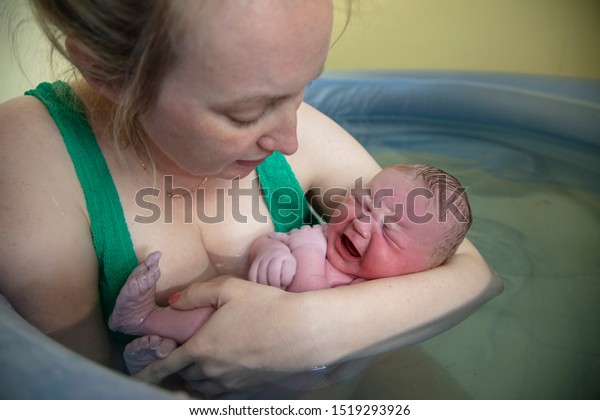 A new mother embracing her newborn baby after a\
natural pool home birth
